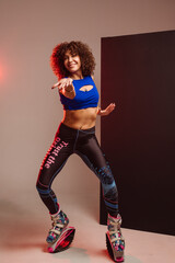 Sporty slim woman in leggings and top wearing kangoo jumper and posing in studio on background - 718041281