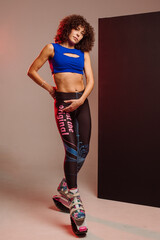 Sporty slim woman in leggings and top wearing kangoo jumper and posing in studio on background - 718041287