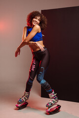 Sporty slim woman in leggings and top wearing kangoo jumper and posing in studio on background - 718041425