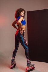 Beautiful sporty woman with curly hair in kangoo jumpers on studio background