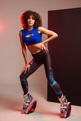Sporty slim woman in leggings and top wearing kangoo jumper and posing in studio on background - 718041437