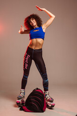 Curly woman in sportswear and bag wearing kangoo jumpers posing in studio on background - 718041455