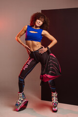 Curly woman in sportswear and bag wearing kangoo jumpers posing in studio on background - 718041495