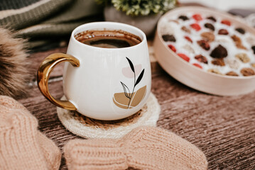 Cup of coffee with autumn leaves and knitted scarf on wooden background