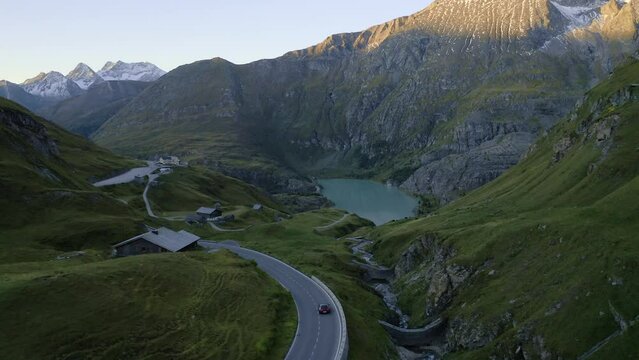Amazing road in the mountains. An aerial shot of a car driving on twisty alpine roads with a breathtaking mountain valley view in the background. Concept of a road trip and luxury travel.
