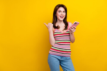 Photo of excited girl dressed striped top look at sale in eshop empty space hold smartphone isolated on vibrant yellow color background