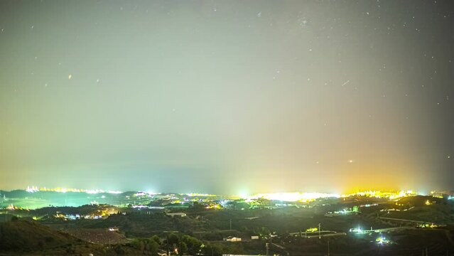 Night city glow and majestic Milky Way galaxy above. Light pollution. Time lapse