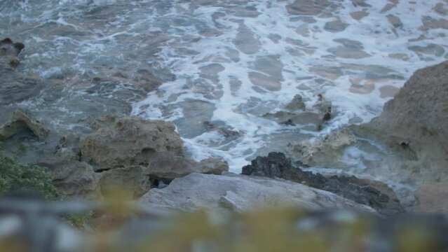 Closeup shot of continuous small tides hitting stones at the shoreline during daytime.
