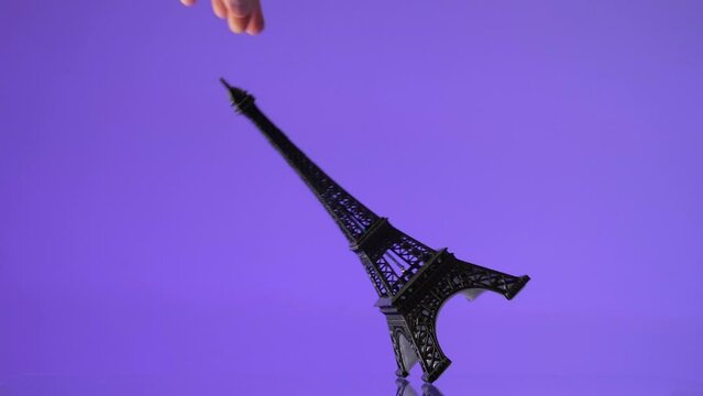 Miniature replica of the Eiffel Tower falling down against a purple background. 