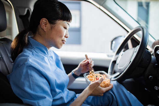 Young asian nurse eating lunch in the car