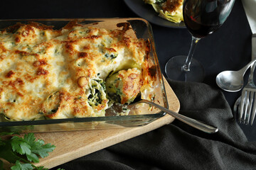 Cannelloni al forno con spinaci, ricotta, besciamella e parmigiano grattugiato su fondo scuro. Cibo...