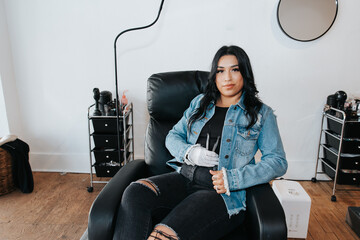 Hispanic woman in a salon chair, confidently holding eyelash tools