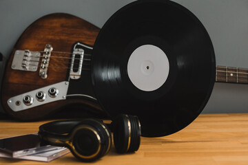 Musical still life, bass guitar, vinyl record and headphones, on a wooden table.