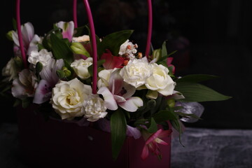 Bouquet of different flowers in a pink box on a dark background