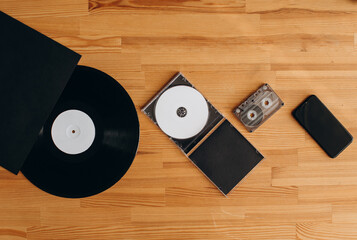 Vinyl record, sd disk, cassette and mobile phone lie on a wooden background. top view
