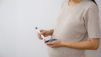 An image of a pregnant woman checking her blood sugar levels at home using a glucometer and blood...