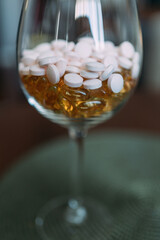 Round tablets of light pink color in a glass and transparent capsules of yellow color. Taking vitamins to improve health and well-being. Dietary supplements on the recommendation of a doctor