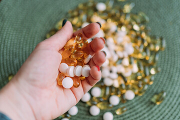 Different vitamins in the palm of a woman's hand. Yellow transparent capsules of different sizes and light pink tablets. There are many similar pills in the background. Vitamins for youth and health