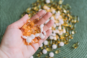 Different vitamins in the palm of a woman's hand. Yellow transparent capsules of different sizes and light pink tablets. There are many similar pills in the background. Vitamins for youth and health