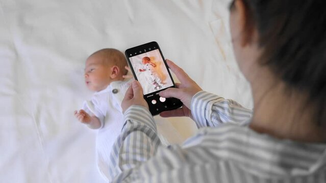Young mother takes a picture of her newborn baby on mobile phone. Baby's photo on cellphone screen