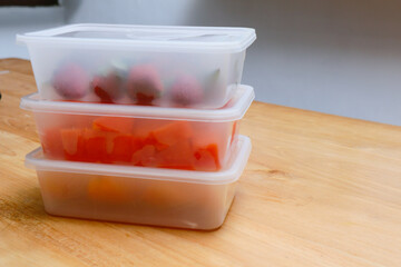 plastic containers containing papaya, strawberries and oranges, on a wooden background