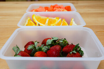 plastic containers containing papaya, strawberries and oranges, on a wooden background