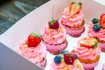 Festive pink cupcakes with fresh strawberries, raspberries and blueberries on cardboard box with chopped pistachios on the top