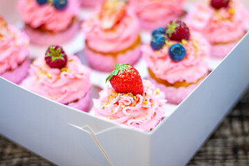 Festive pink cupcakes with fresh strawberries, raspberries and blueberries on cardboard box with...