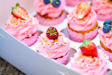 Festive pink cupcakes with fresh strawberries, raspberries and blueberries on cardboard box with chopped pistachios on the top