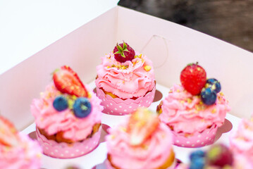 Festive pink cupcakes with fresh strawberries, raspberries and blueberries on cardboard box with chopped pistachios on the top