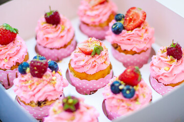 Festive pink cupcakes with fresh strawberries, raspberries and blueberries on cardboard box with chopped pistachios on the top