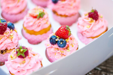 Festive pink cupcakes with fresh strawberries, raspberries and blueberries on cardboard box with chopped pistachios on the top