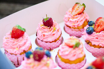 Festive pink cupcakes with fresh strawberries, raspberries and blueberries on cardboard box with chopped pistachios on the top