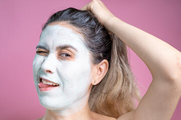 Fototapeta premium Portrait of a woman with a cosmetic mask on her face. A cheerful woman with a white face.