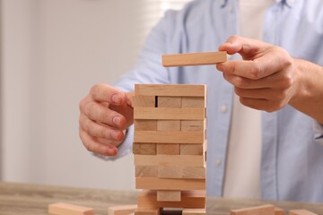 Playing Jenga. Man building tower with wooden blocks at table, closeup