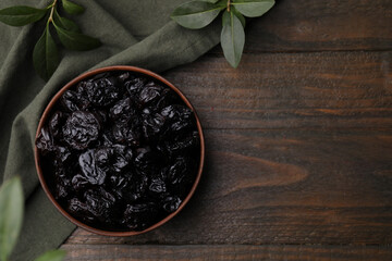 Sweet dried prunes in bowl on wooden table, top view. Space for text