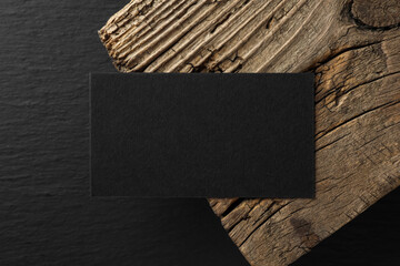 Empty business card and piece of wood on black background, top view. Mockup for design