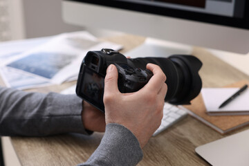 Professional photographer with digital camera at wooden table indoors, closeup