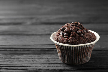 Delicious chocolate muffin on black wooden table, closeup. Space for text