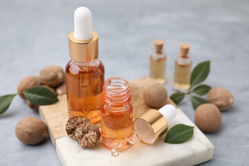 Fototapeta na wymiar Nutmeg essential oil, nuts and leaves on light grey table, closeup