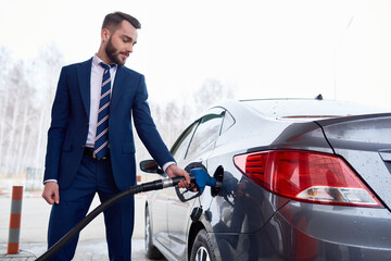 Side view at man wearing suit while refueling gas tank of car in petrol station, copy space - obrazy, fototapety, plakaty