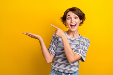 Photo of overjoyed impressed woman dressed striped t-shirt directing at product on palm empty space isolated on yellow color background - obrazy, fototapety, plakaty