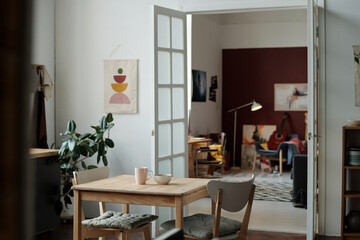 Part of spacious living room with square wooden table and two chairs standing in the center against open door and interior