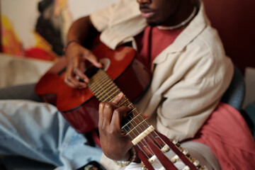 Hand of young unrecognizable African American man playing acoustic string musical instrument while...