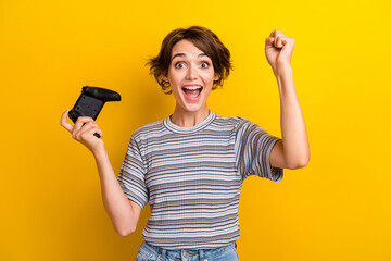 Photo of ecstatic satisfied woman dressed striped t-shirt raising up playstation joystick win game isolated on yellow color background