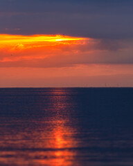 Naklejka na ściany i meble Vibrant red sunrise shining through a cloud bank over the sea. Wind farm turbines far in the distance - Beaumaris North Wales