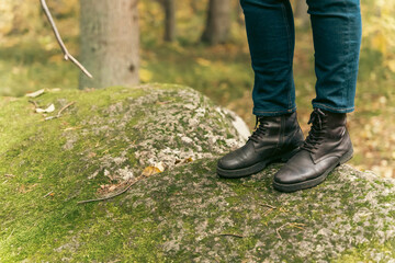 women's feet in leather autumn boots and jeans stand on the green forest moss