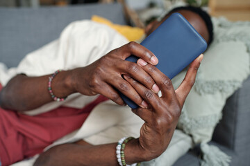 Hands of young unrecognizable African American man with smartphone in front of camera lying on...