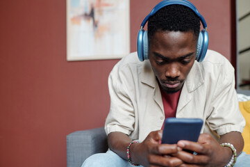 African American guy in headphones looking through playlist while sitting in front of camera and...