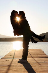 Ein Paar küsst sich bei Sonnenuntergang auf einem Steg am Wasser